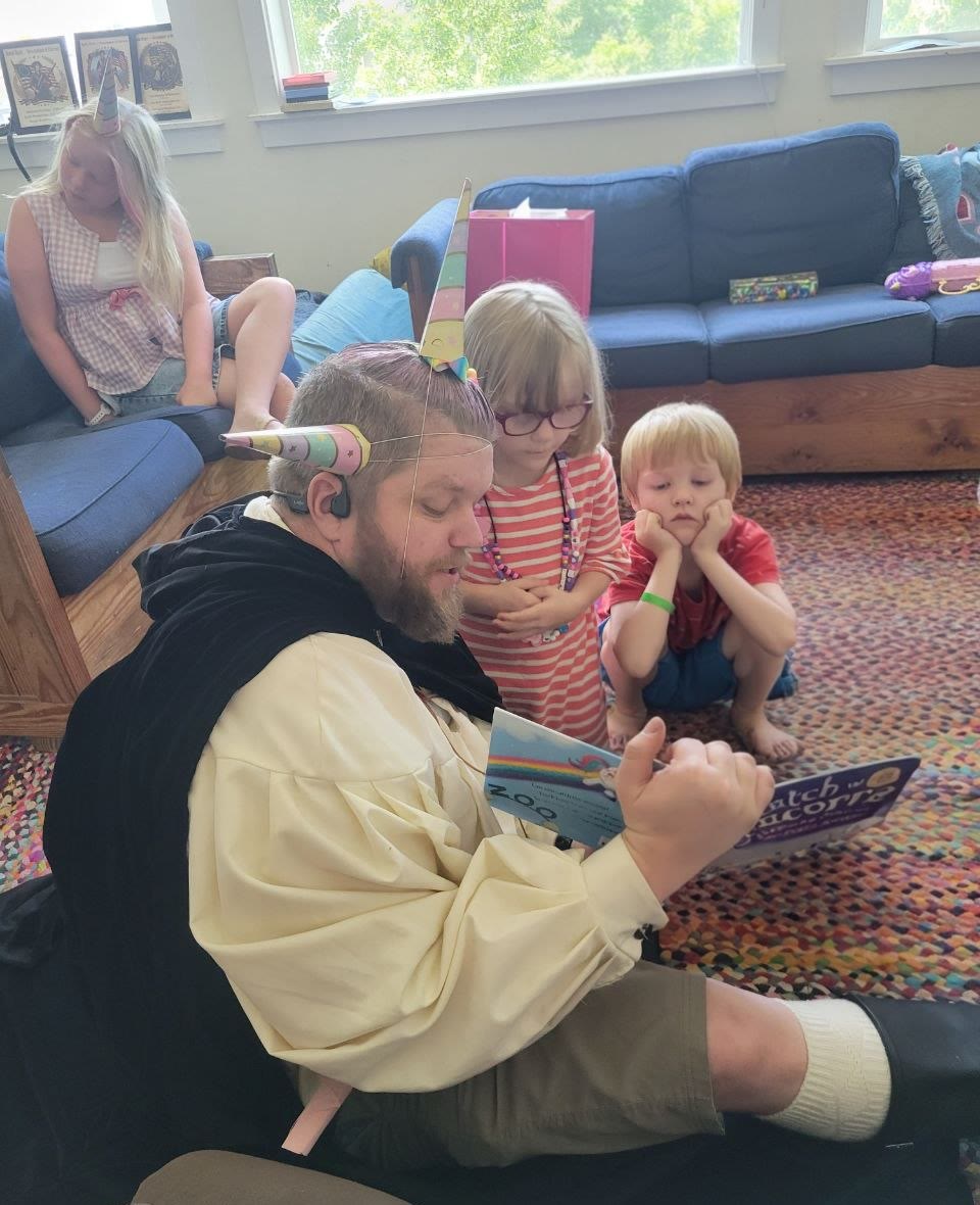 Costumed storyteller in a unicorn horn reading Catch a Unicorn to captivated kids